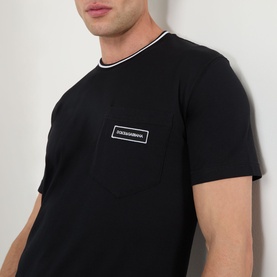 Model wearing Dolce & Gabbana black cotton T-shirt with white tipped crew neck and chest logo patch.