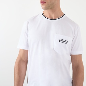 Model wearing Dolce & Gabbana Tipped Logo T-Shirt in Optical White, showing chest pocket with logo badge and contrast tipped neckline.
