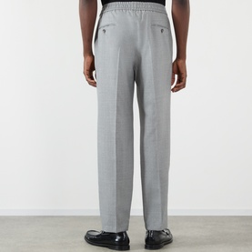 Model wearing Dolce & Gabbana grey melange wool trousers, rear view, elasticated waistband, straight leg, styled with black loafers.