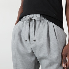 Model wearing Dolce & Gabbana grey melange wool trousers, styled with a black T-shirt. Elasticated waistband with drawstring tie detail.