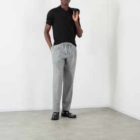 Model wearing Dolce & Gabbana Grey Melange virgin wool trousers with drawstring waist, styled with black polo shirt and black loafers.