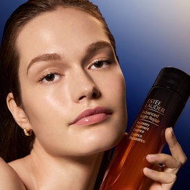 Model with Est&eacute;e Lauder Advanced Night Repair Recovery Treatment Lotion, holding the amber bottle close to face, wearing gold hoop earrings.