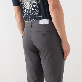 Model wearing Farah Vintage Charcoal Chino trousers, rear view showing back pockets, styled with a navy graphic T-shirt.