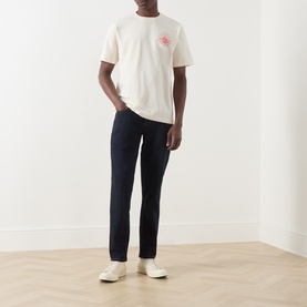 Model wearing Farah Vintage Ecru Crew Neck T-Shirt with small chest graphic, styled with navy trousers and white trainers.