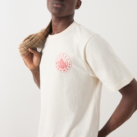 Model wearing Farah Vintage Ecru Crew Neck T-shirt with red circular chest logo, styled with a checked jacket over the shoulder.