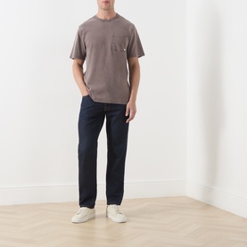 Model wearing Farah Vintage Dark Brown crew neck cotton T-shirt with chest pocket, styled with dark indigo jeans and white trainers.