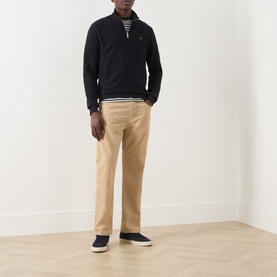 Model wearing Farah Vintage Navy Half Zip sweatshirt with beige chinos, striped tee visible at collar, and navy canvas shoes.