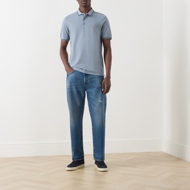 Model wearing Farah Vintage Icelandic Blue cotton polo shirt with tipped collar, styled with mid-blue distressed jeans and dark trainers.