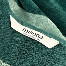 Misona Beach Towel in green blue, 100% organic cotton, close-up showing woven label detail and textured terry fabric.