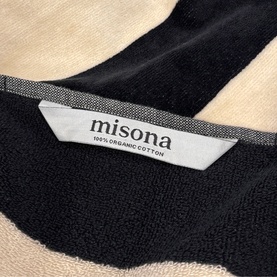 Misona Beach Towel Natural Black, close-up of woven label on black and natural cotton terry fabric, 100% organic cotton