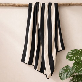 Misona Beach Towel Natural Black, 100% cotton jacquard with bold black and cream vertical stripes, draped over a wooden pole.