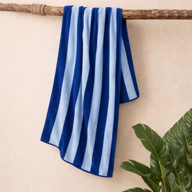 Misona Beach Towel Navy Sky in navy and light blue stripes, 100% cotton, draped over a wooden pole with tropical leaf backdrop.