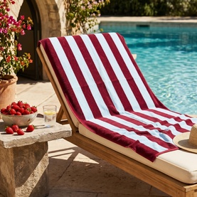 Misona Beach Towel Red Sky draped over a wooden sun lounger by a pool, bold red and white vertical stripes, 100% cotton jacquard