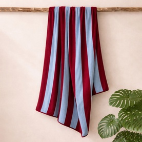 Misona Beach Towel Red Sky in bold red and pale blue vertical stripes, 100% cotton, draped over a wooden rail.