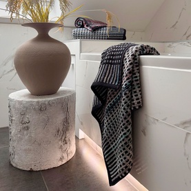 Odyssey Carnival Towel Black, 100% cotton jacquard beach towel with geometric pattern, draped over bath in marble bathroom setting