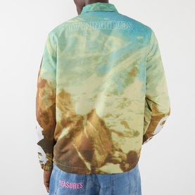 Model wearing Pleasures multi-colour all-over landscape print casual jacket, shown from the back, paired with denim jeans.