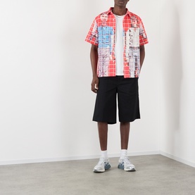 Model wearing Pleasures More Songs About Buildings and Food Check Shirt in red graphic check print, styled with black shorts and white trainers.