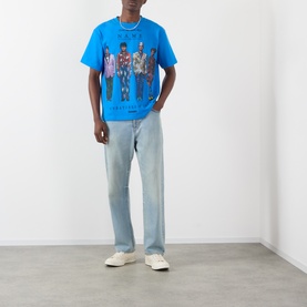 Model wearing Pleasures Creatures of Love Logo Graphic T-Shirt in blue with light wash jeans and white trainers.