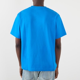 Model wearing Pleasures Creatures of Love Logo Graphic T-Shirt in blue, back view, with light wash jeans.