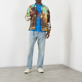 Model wearing Pleasures Creatures of Love Logo Graphic T-Shirt in blue, styled with a multicolour printed jacket and light wash jeans.