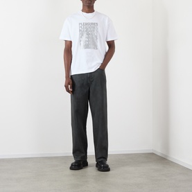 Model wearing Pleasures Immolate Logo Graphic T-Shirt in white with graphic print, styled with dark wide-leg trousers and black loafers.