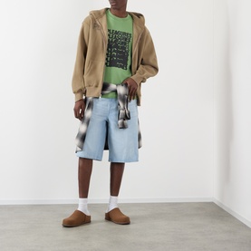 Model wearing Pleasures Immolate Logo Graphic T-Shirt in Sage, styled with tan zip hoodie, light-wash denim shorts, and brown suede loafers.