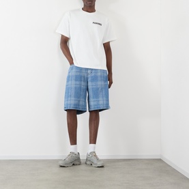 Model wearing Pleasures Impact Logo Graphic T-Shirt in white with blue check shorts and grey trainers.