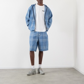 Model wearing Pleasures Impact Logo Graphic T-Shirt in white, styled with blue plaid shorts and matching zip hoodie, white socks and grey trainers.