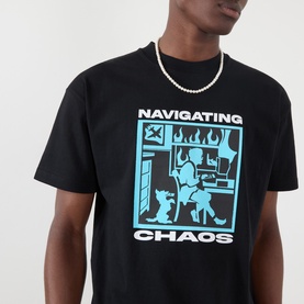 Model wearing Pleasures Navigating Chaos Logo Graphic T-Shirt in black with cyan chest print, styled with a pearl chain necklace.