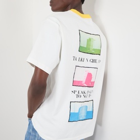 Model wearing Pleasures Speaking Logo Graphic T-Shirt in white with colourful pop-art print panels on back and contrast yellow collar.