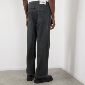 Model wearing Pleasures black wide-leg jeans, rear view, with black chunky sole shoes. Relaxed fit, 100% cotton denim.