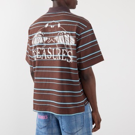 Model wearing Pleasures brown striped polo shirt with back graphic print, styled with blue jeans