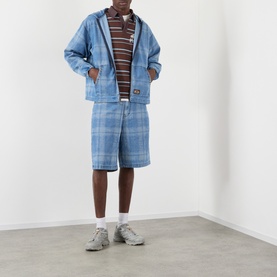 Model wearing Pleasures brown striped polo with blue check shorts, denim jacket, white socks and grey trainers.