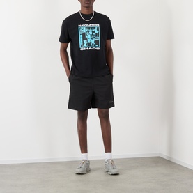 Model wearing Pleasures Active Striped Shorts in black with elasticated waist and logo detail, styled with black graphic tee and grey trainers.