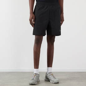 Model wearing Pleasures Active Striped Shorts in black with elasticated waist, styled with white socks and grey chunky trainers.