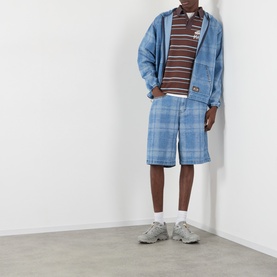 Model wearing Pleasures blue check shorts, styled with matching denim jacket, striped polo shirt and grey chunky trainers