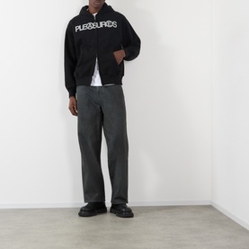 Model wearing Pleasures Zine Logo Zip Hoodie in black with grey wide-leg trousers and black loafers.