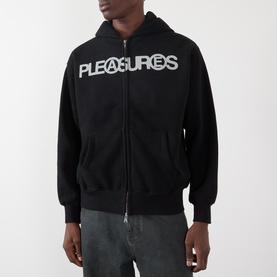 Model wearing Pleasures Zine Logo Zip Hoodie in black with white logo print, styled with grey jeans.