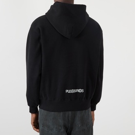 Model wearing Pleasures Zine Logo Zip Hoodie in black, rear view showing logo print, styled with dark grey jeans.