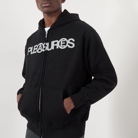 Model wearing Pleasures Zine Logo Zip Hoodie in black with contrast logo print, zip fastening, and split pouch pocket.