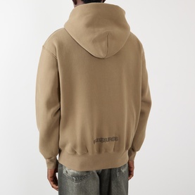 Model wearing Pleasures Zine Logo Zip Hoodie in beige, rear view showing logo detail, styled with distressed denim jeans.