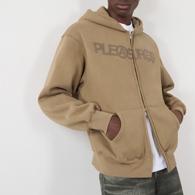 Model wearing Pleasures Zine Logo Zip Hoodie in beige with tonal logo print, zip fastening and split pouch pocket, styled with white tee and khaki