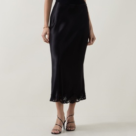 Model wearing Rixo London black viscose midi skirt with lace hem trim, styled with black strappy heeled sandals.