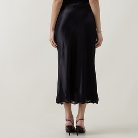 Model wearing Rixo London black viscose midi skirt with lace hem trim, shown from behind, styled with black strappy heels.