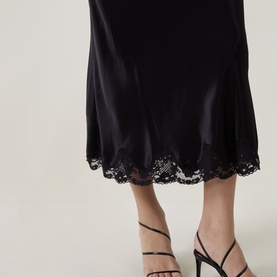 Model wearing Rixo London black viscose midi skirt with lace hem trim, styled with black strappy heeled sandals.