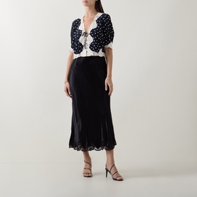 Model wearing Rixo London black viscose midi skirt with lace hem trim, styled with a polka dot top and strappy heels.