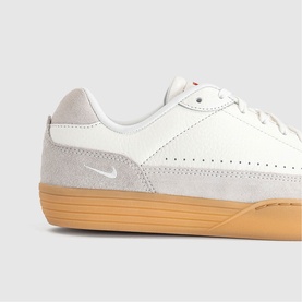 Nike trainer in sail white with light grey suede overlay, small swoosh logo, and honey gum rubber sole. Close-up detail shot.