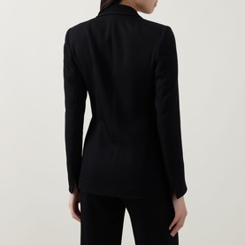 Model wearing Akris Punto black blazer, rear view, fitted silhouette with tailored seams, styled with matching black trousers.