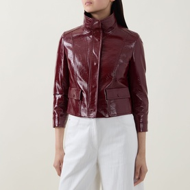 Model wearing Akris Punto pomegranate patent croc-effect structured jacket with high collar, styled with white wide-leg trousers.