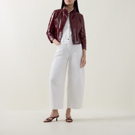 Model wearing Akris Punto pomegranate patent leather jacket styled with white wide-leg trousers and strappy heeled mules.